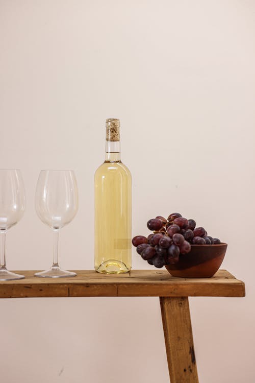 Bottle of White Wine and Bowl of Grapes on a Wooden Table