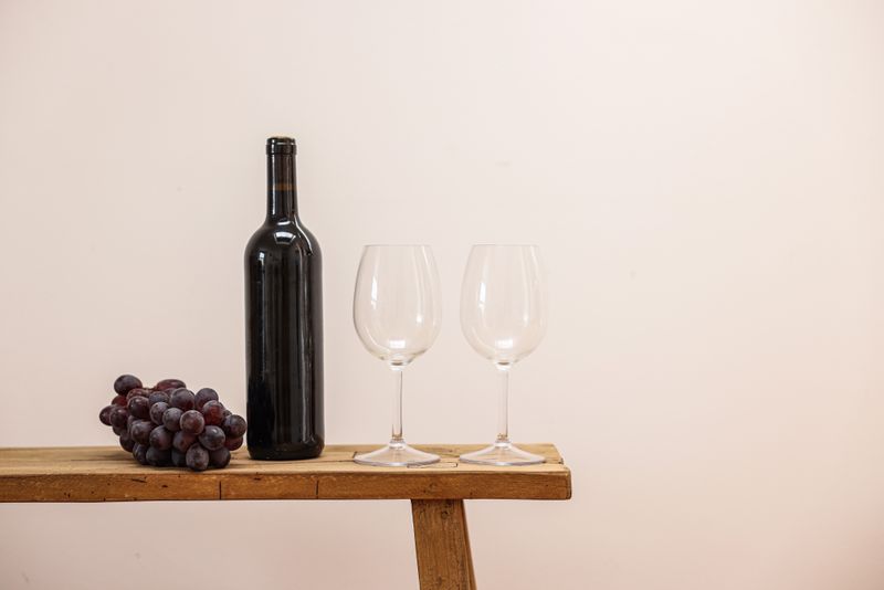 Bottle of red wine with two glasses on a wooden bench — photo by Cup of Couple on Pexels