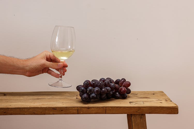 Person Holding Wine Glass Beside Grapes