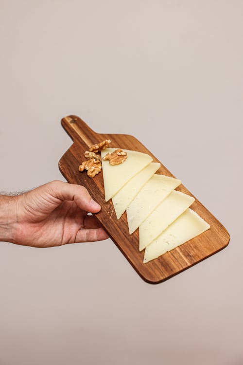 A Hand Holding a Wooden Chopping Board with Cheese Slices