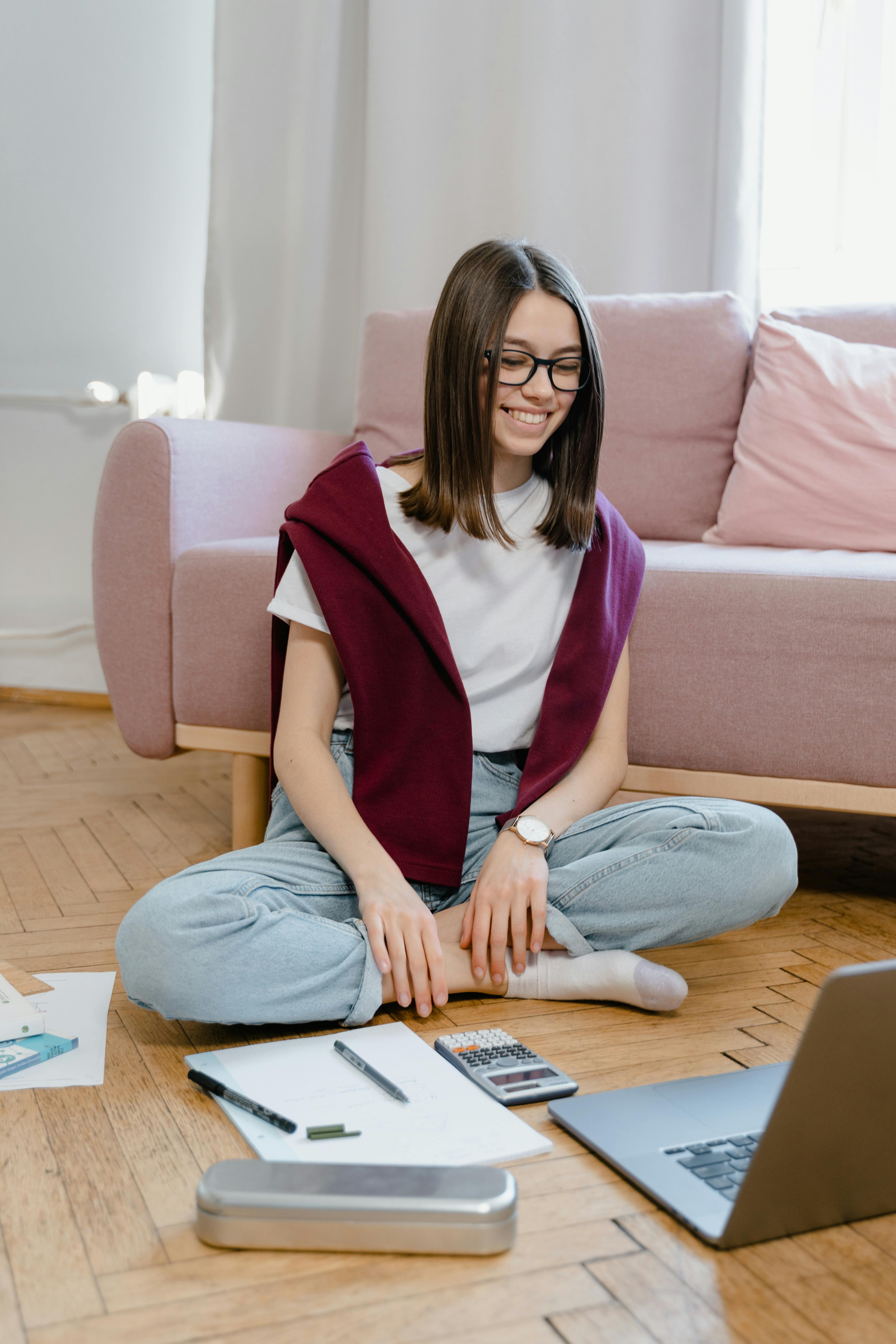 a happy young woman sitting on the floor while taking an online class