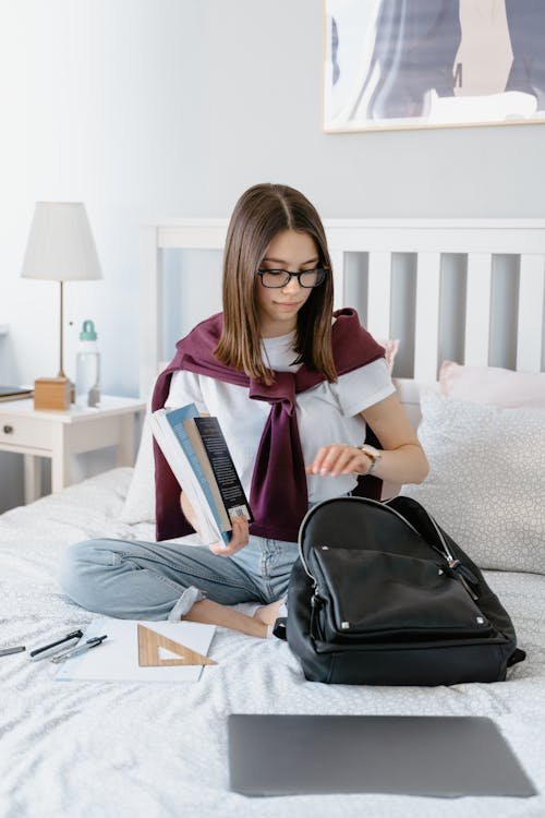 Free A Young Woman Packing her Books while Sitting on the Bed Stock Photo