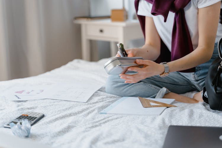 A Student Holding A Pencil Case While Sitting On A Bed