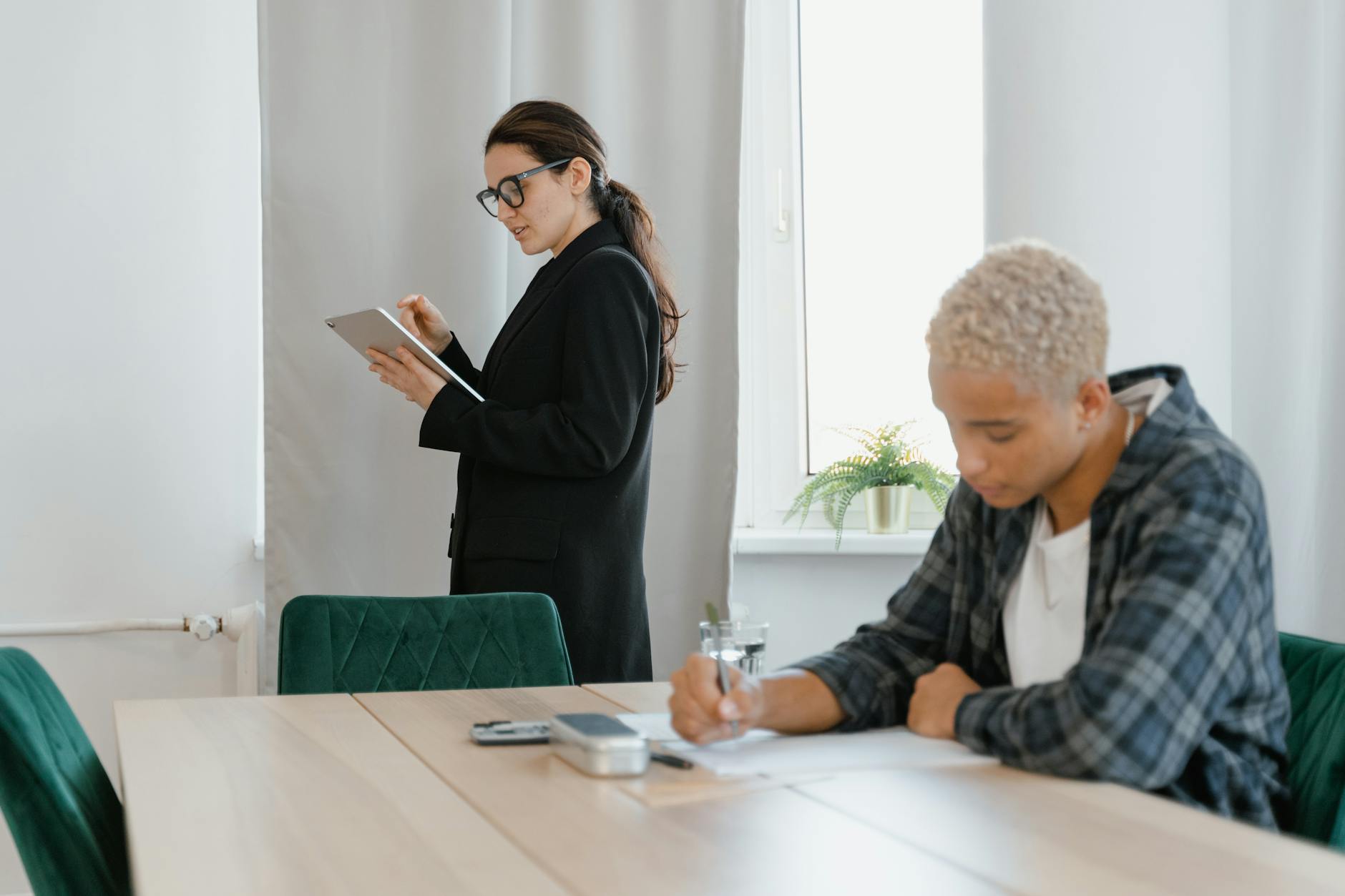 A teacher with a tablet monitors a student writing during a lesson in a modern classroom.