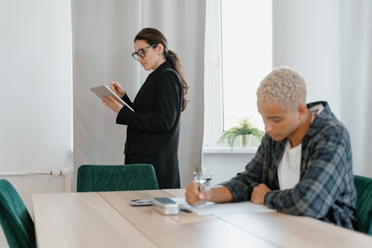 A teacher with a tablet monitors a student writing during a lesson in a modern classroom.