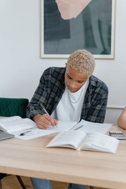 Teen student writing at home desk, surrounded by open books, engaged in study. Teen student writing at home desk, surrounded by open books, engaged in study.