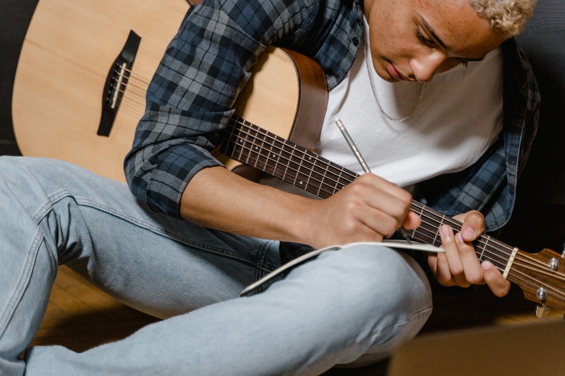 Guitarrista estudia los tips de producción musical, escribe en un papel mientras sostiene su guitarra