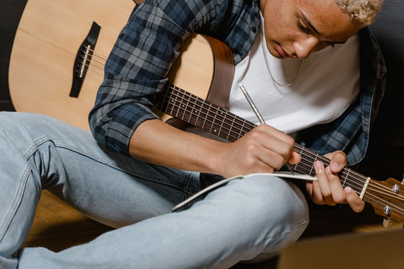 A man in a plaid shirt writing a song on an acoustic guitar in warm light