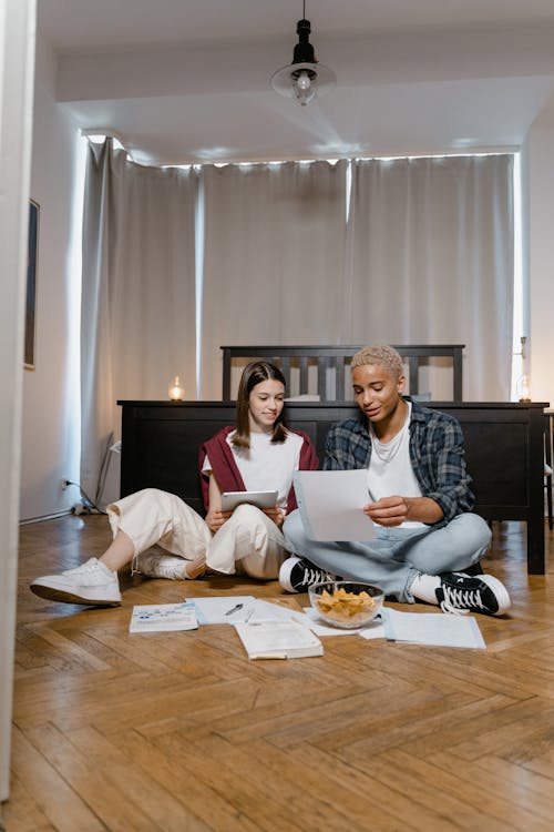 Man and Woman Sitting on Wooden Floor and Studying Together
