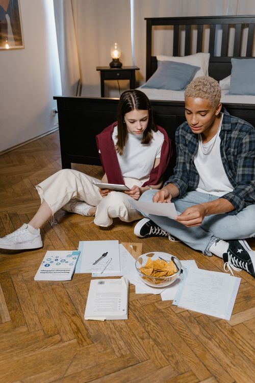 Free Two young adults sit on the floor studying, surrounded by papers and snacks. Stock Photo
