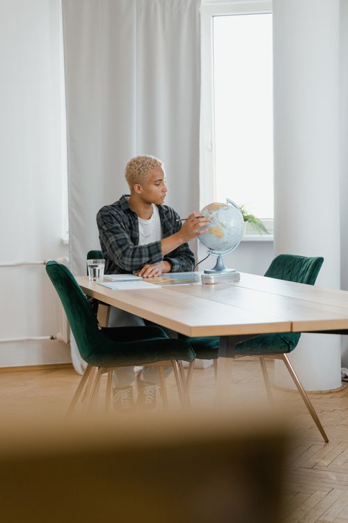 Free Young adult points at globe while studying indoors at a table, emphasis on education. Stock Photo