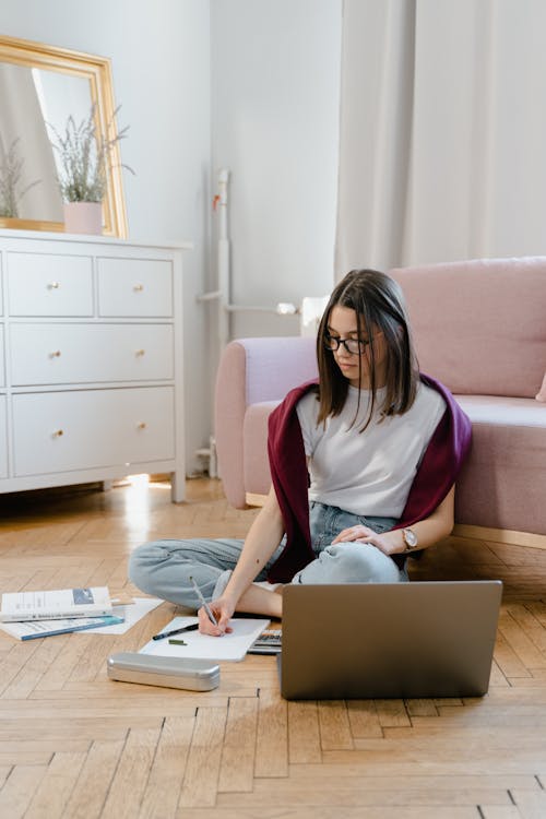 A Young Woman Sitting on the Floor while Taking an Online Class