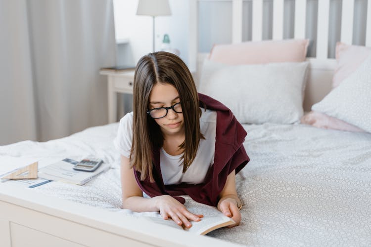 A Young Woman Reading A Book On A Bed