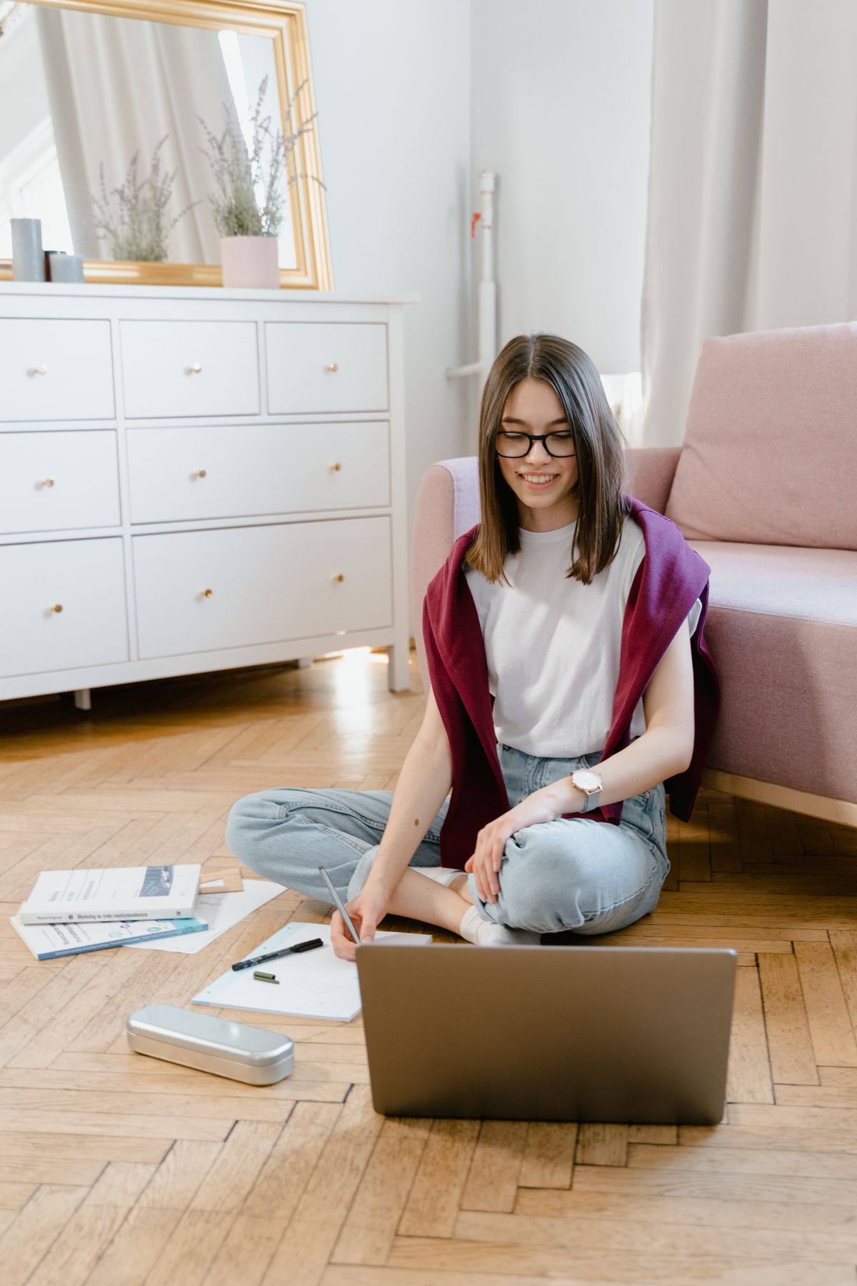 Happy young woman taking an online class on a laptop while sitting on the floor at home
