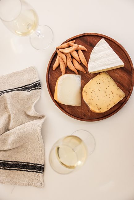 Sophisticated cheese selection with wine glasses on a wooden plate. Ideal for gourmet lifestyle visuals.