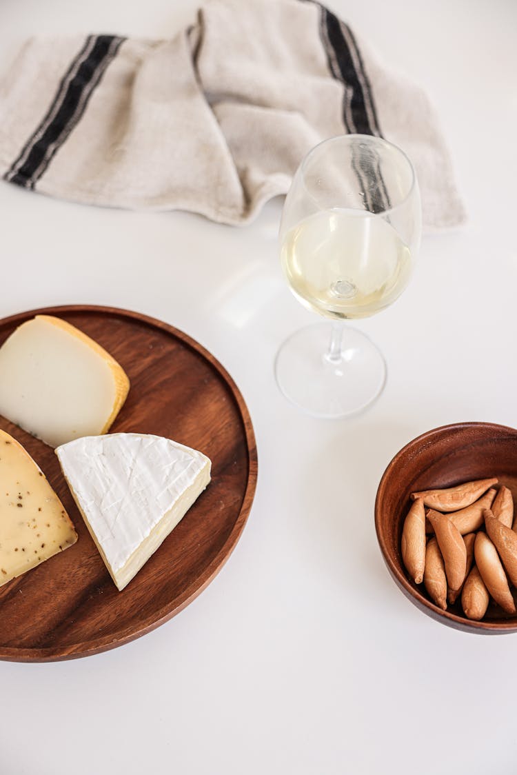 A Glass Of Wine A Cheese Platter On A White Surface