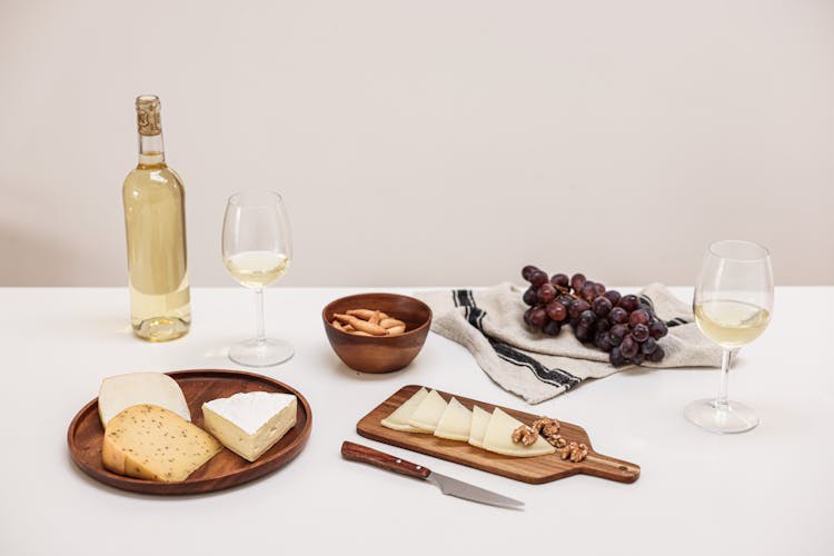 An Assorted Cheese And Grapes On The Table With Wine Glasses