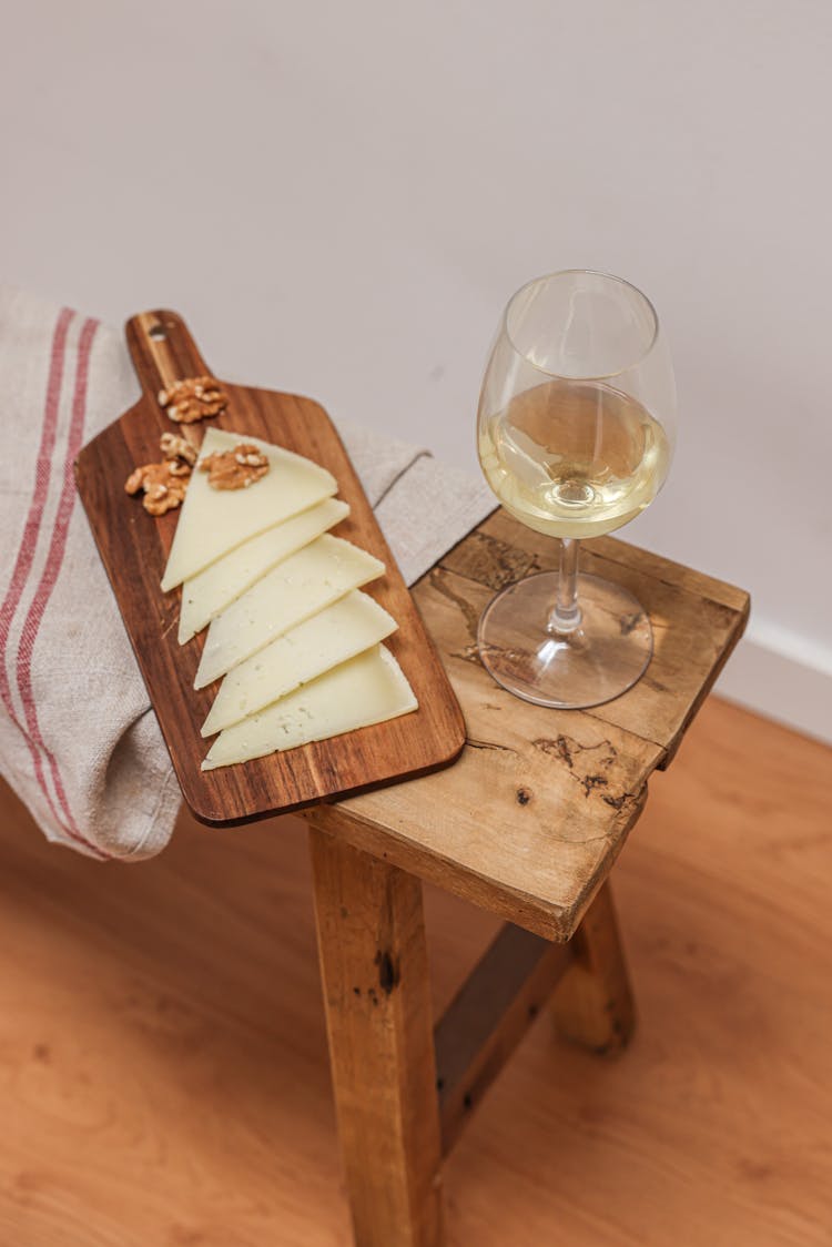 Walnuts And Cheese Slices Beside A Glass Of White Wine