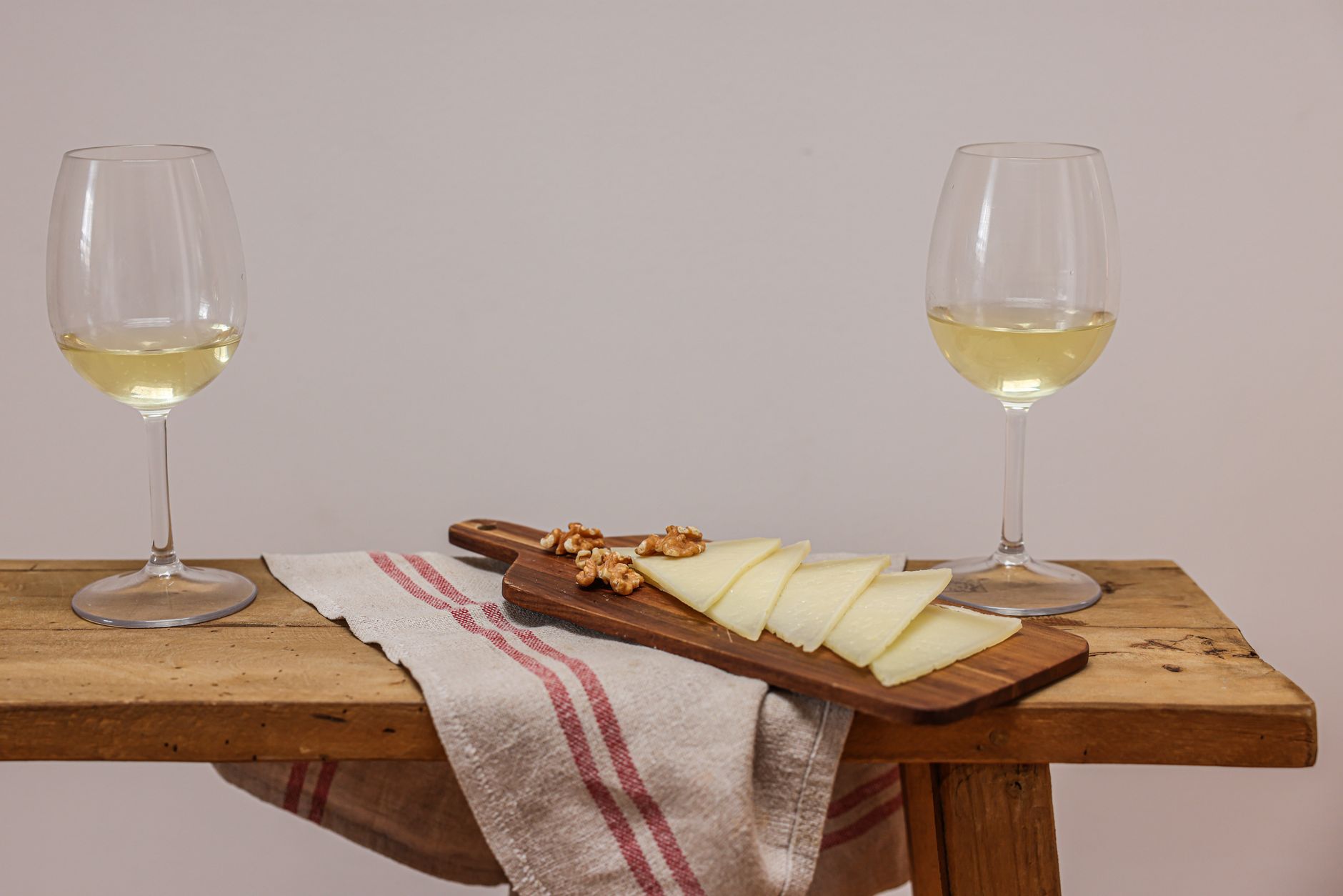 Two glasses of white wine with cheese and walnuts on a wooden board for a cozy gathering.