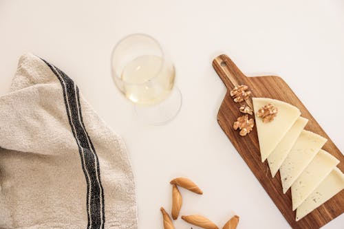 A Wine Glass Near the Wooden Board with Cheese and Walnuts