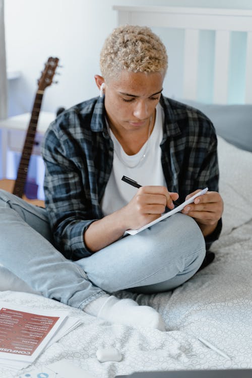 A Young Man Doing his Homework while Sitting on a Bed