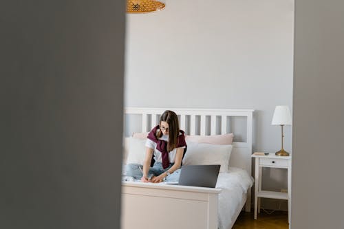 Free A Young Woman Doing her Homework while Sitting on a Bed Stock Photo