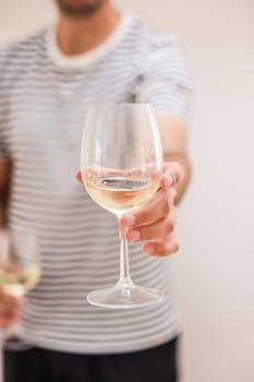 Close-up of a person holding a white wine glass, focus on the wine and hand.