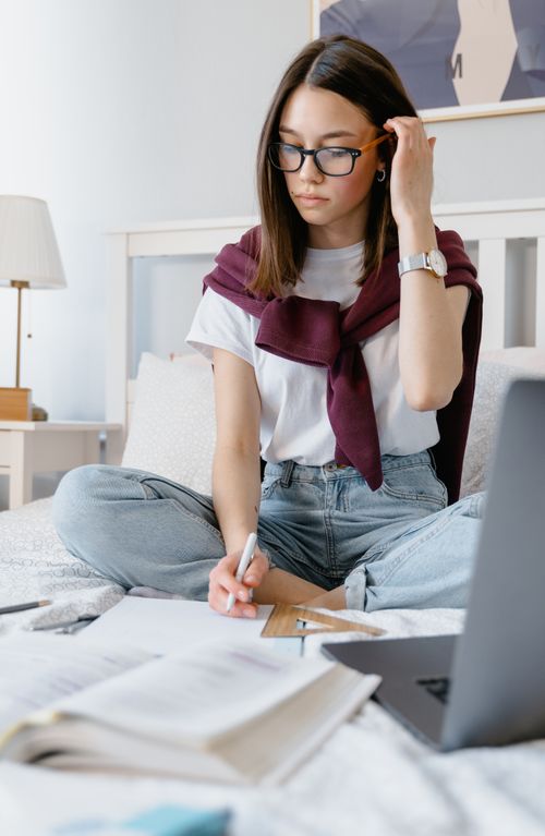 Free Focused young woman studying on bed with laptop, books, and notes. Stock Photo