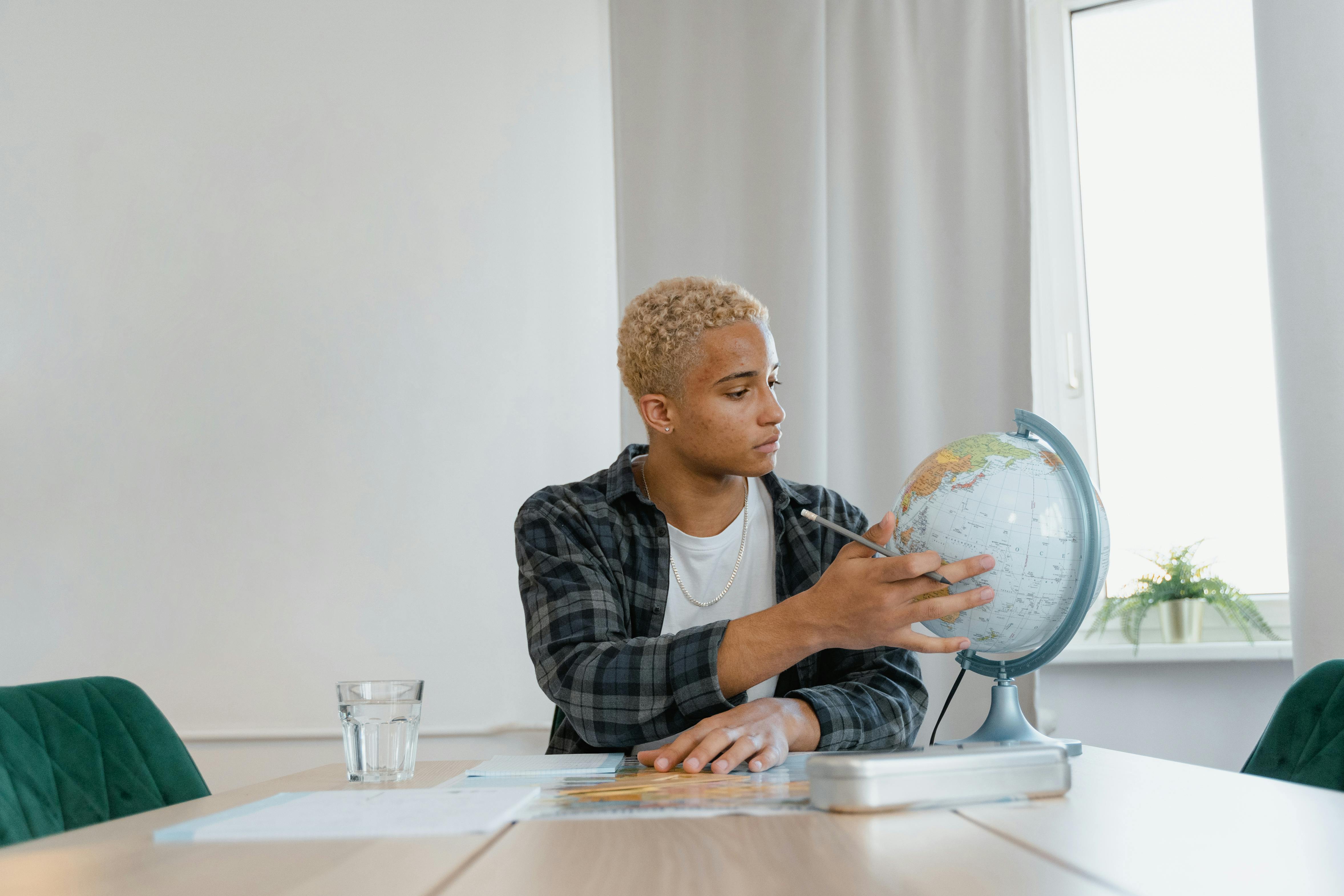 a young man looking at a globe while sitting at a table