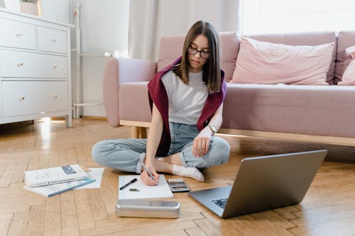 A Young Woman Sitting on the Floor while Taking an Online Class