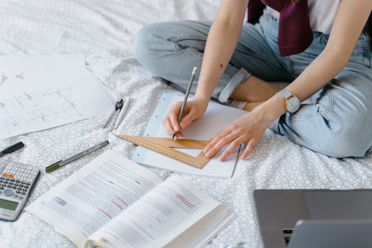 A Student Drawing With A Set Square While Sitting On A Bed