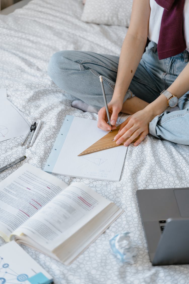 A Student Drawing With A Set Square While Sitting On A Bed