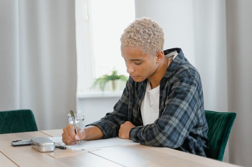 Free Teenager writing at a desk with a focus on homework and study in a home setting. Stock Photo