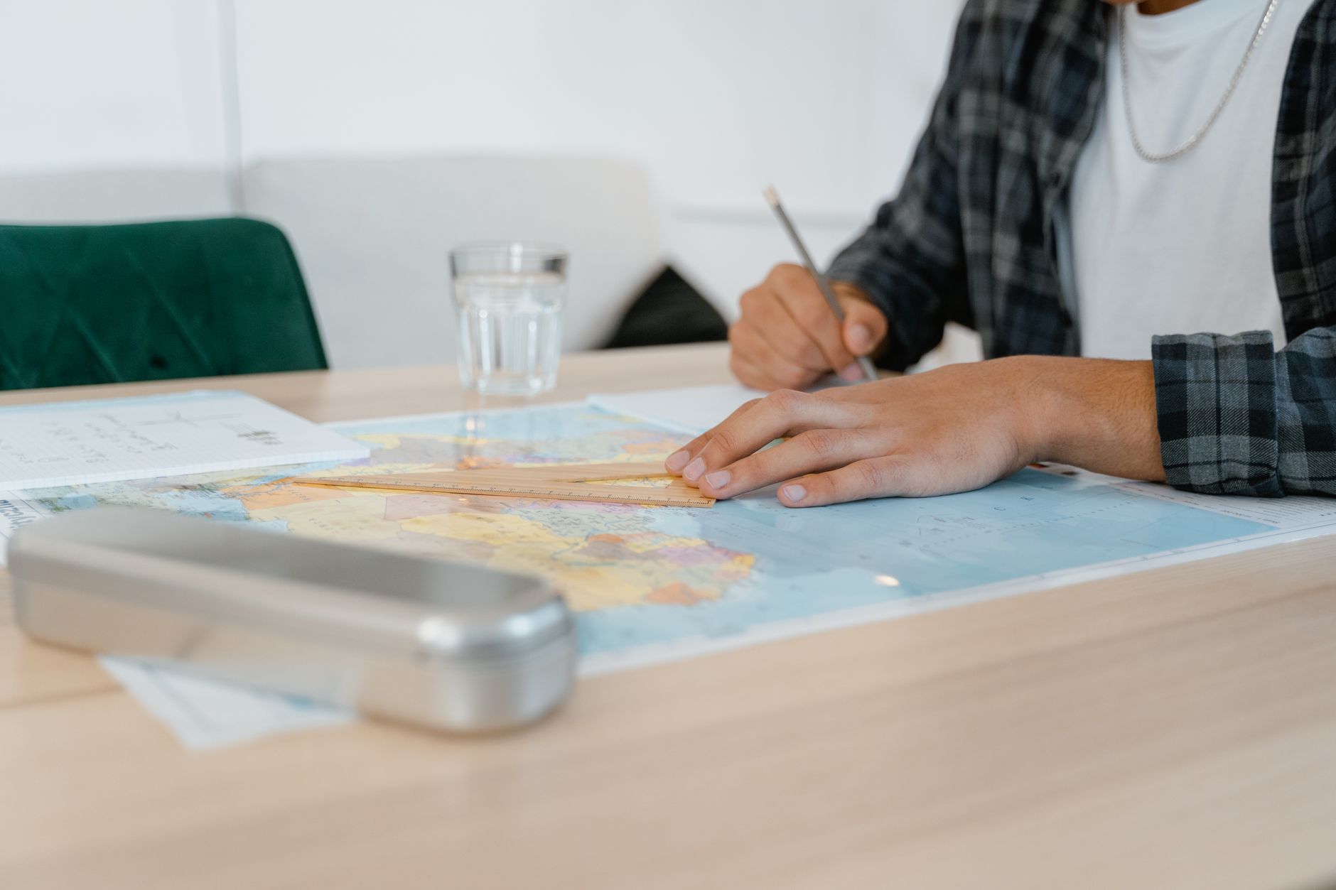 Student using a set square on a world map at a desk, taking notes indoors.