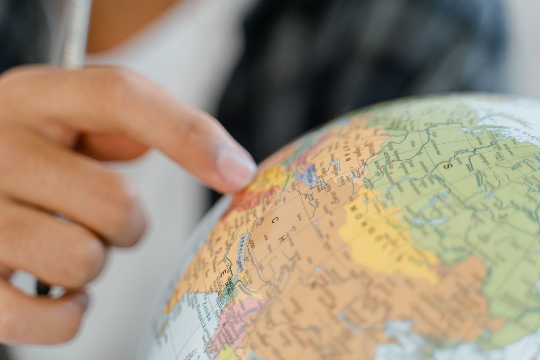A close-up of a hand pointing at a globe, highlighting exploration and travel concepts.
