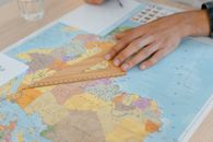 A hand uses a wooden ruler on a world map, focusing on precise measuring.