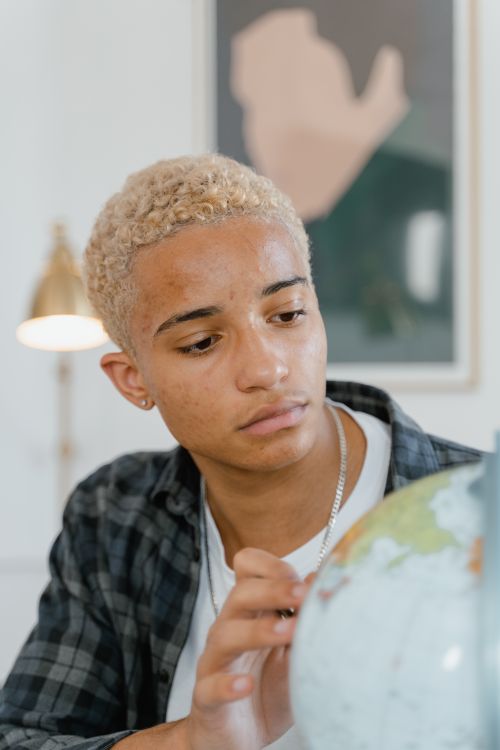 Free Curious young man examines a globe indoors, representing global learning and exploration. Stock Photo