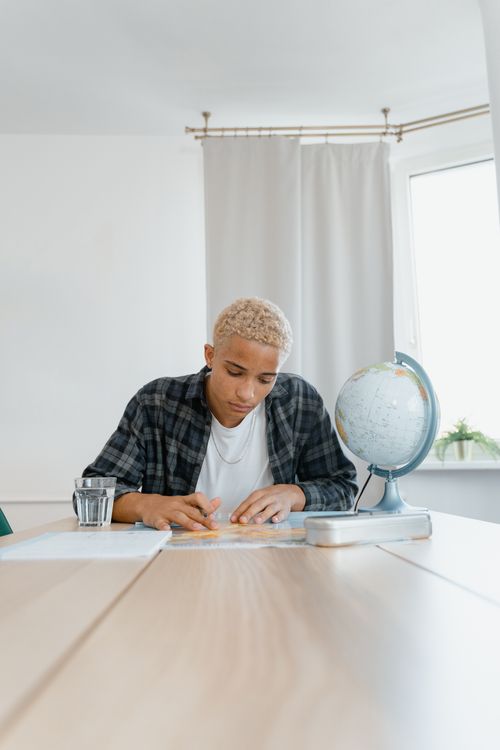 Free Man studying maps with a globe at a table, bright indoor setting, learning concept Stock Photo