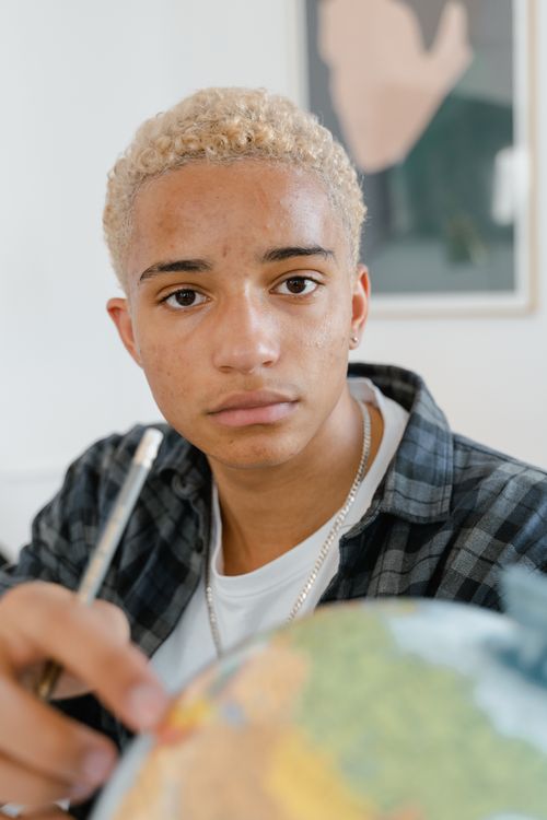 Free Teenage student with a pencil points at a globe indoors, focused expression. Stock Photo