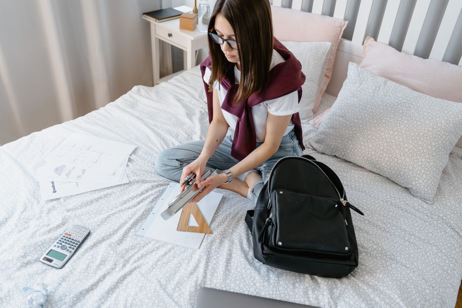 Teen girl organizing school supplies in a bedroom setting, preparing for study.