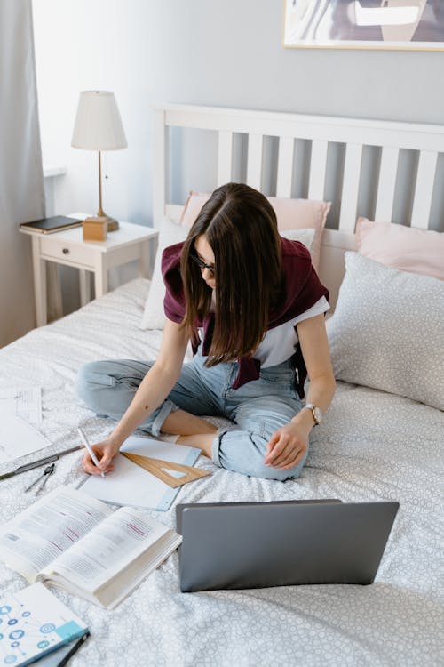 A Young Woman Taking an Online Class While Sitting on a Bed