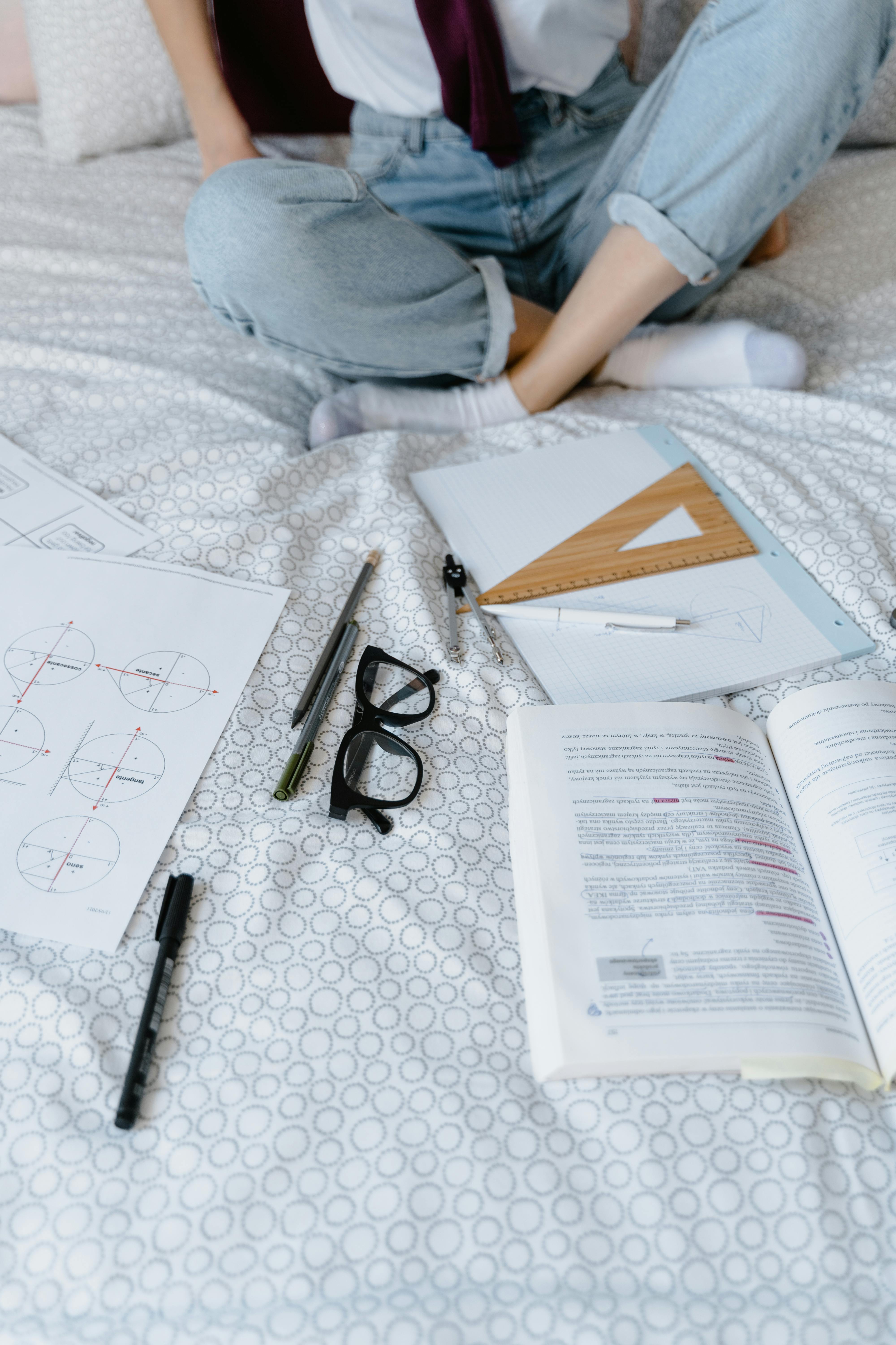 A student studying geometry with worksheets and pens on a bed, highlighting remote learning setup.