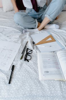 A student studying geometry with worksheets and pens on a bed, highlighting remote learning setup.