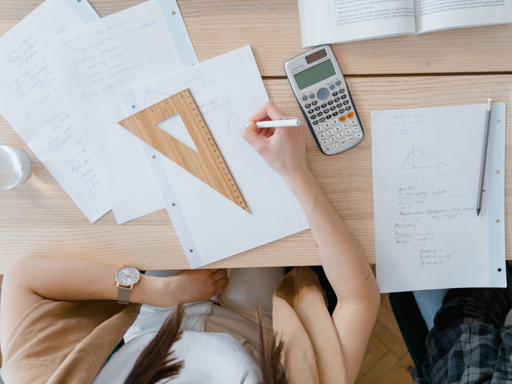 An overhead view of a student studying geometry using a calculator and notes at home. Perfect for education visuals.