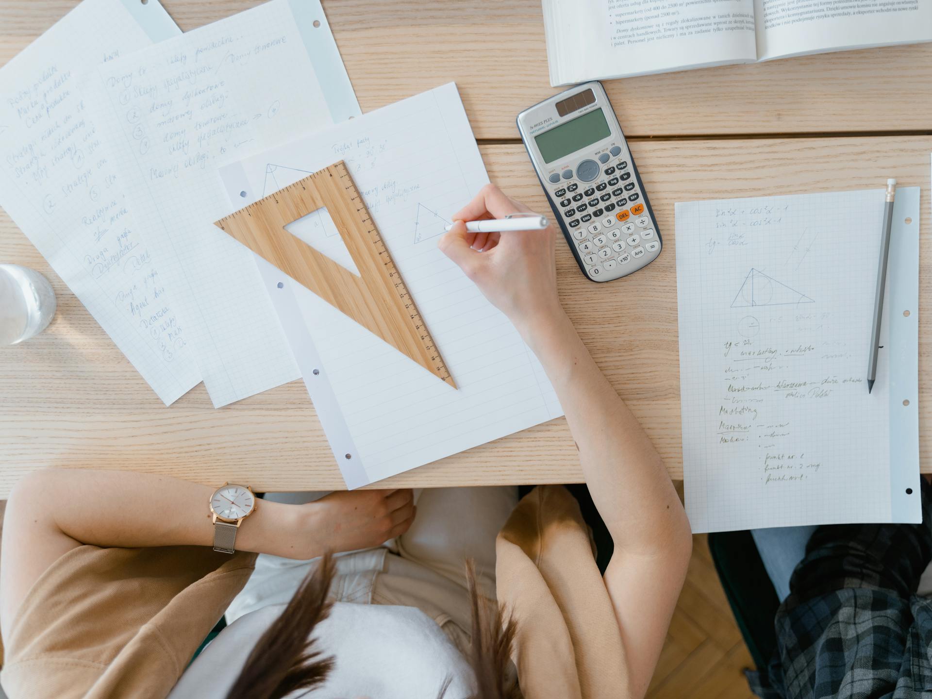 An overhead view of a student studying geometry using a calculator and notes at home. Perfect for education visuals.