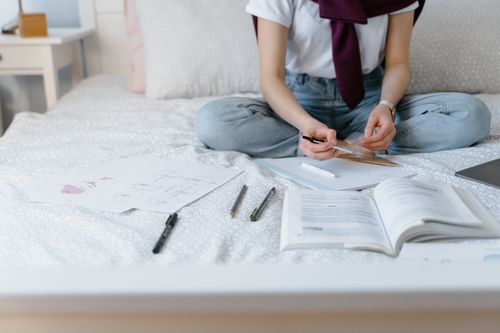 Free A person studying with books and papers on a bed, focusing on homework or home schooling. Stock Photo
