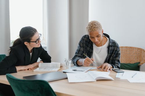 Free Two adults engaged in a focused study session at a home table with books and papers. Stock Photo