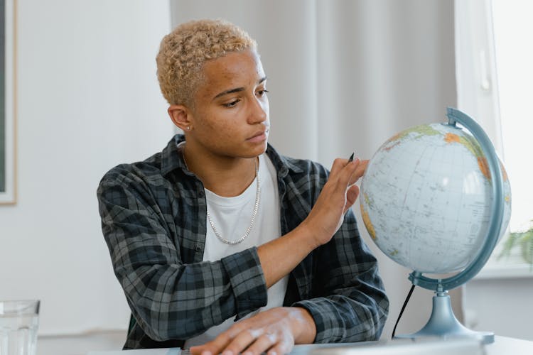 A Man In Plaid Long Sleeves Looking At The Globe