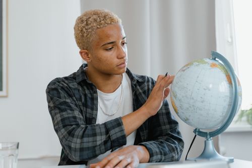 Free A young man indoors examining a globe, symbolizing education and exploration. Stock Photo