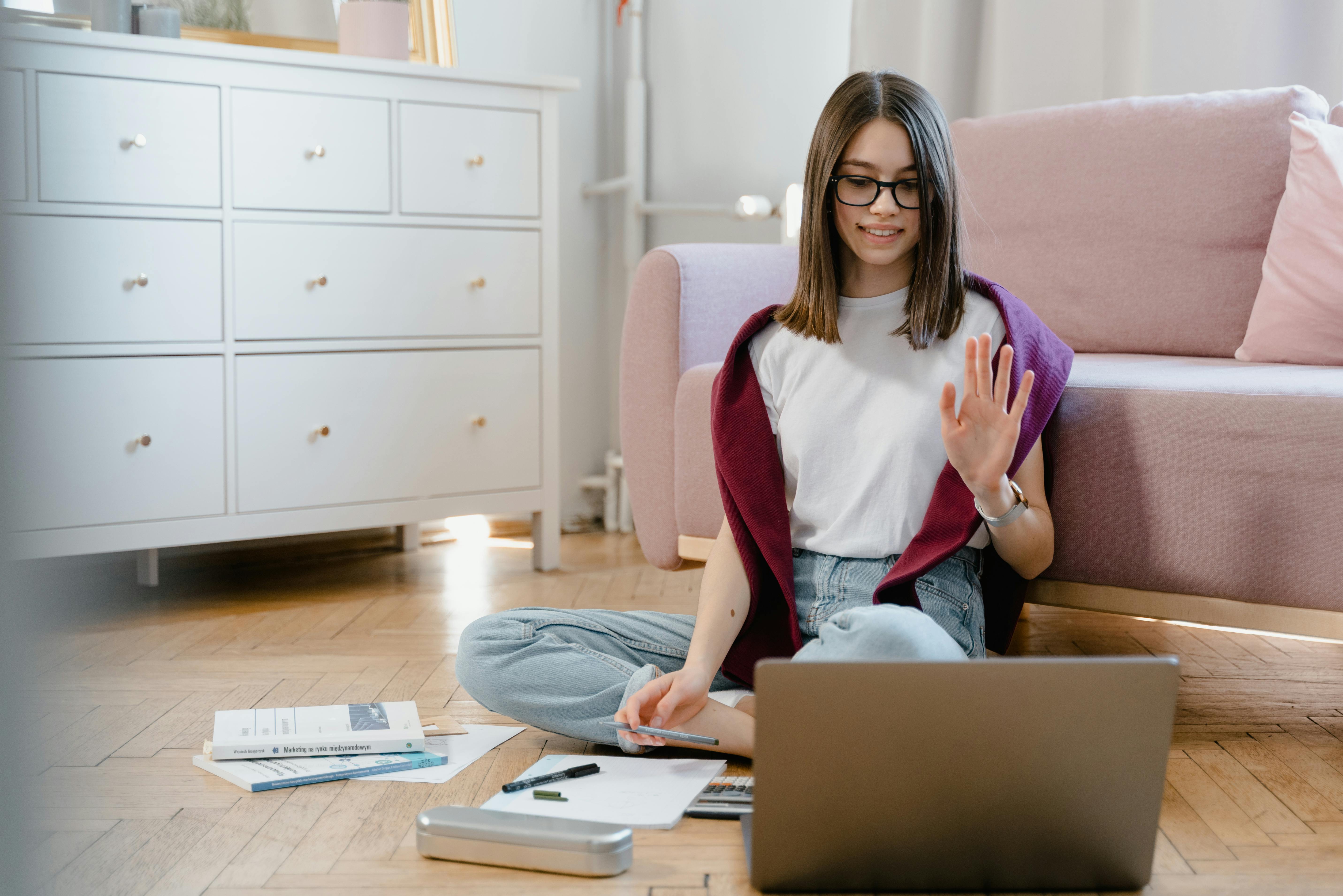 a woman in white shirt sitting on the floor while talking in front of her laptop